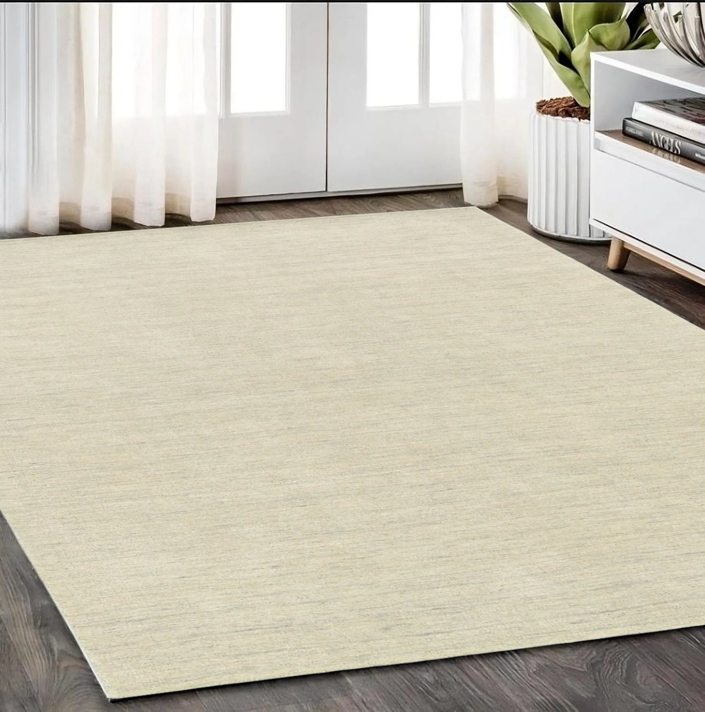 Beige wool area rug on a wooden floor with a white cabinet and plant in the background