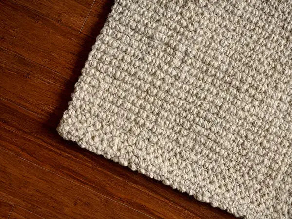 Close-up of a textured ivory rug corner on a wooden floor