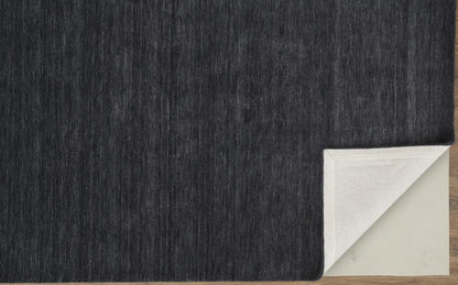 Black wool rug corner with a white border on a wooden floor