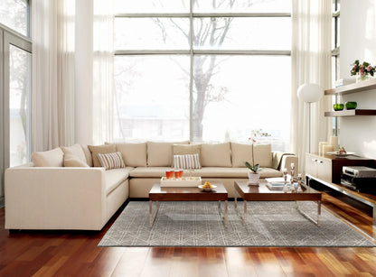 Modern living room with beige sectional sofa, wooden coffee table, large windows and a gray geometric wool rug.