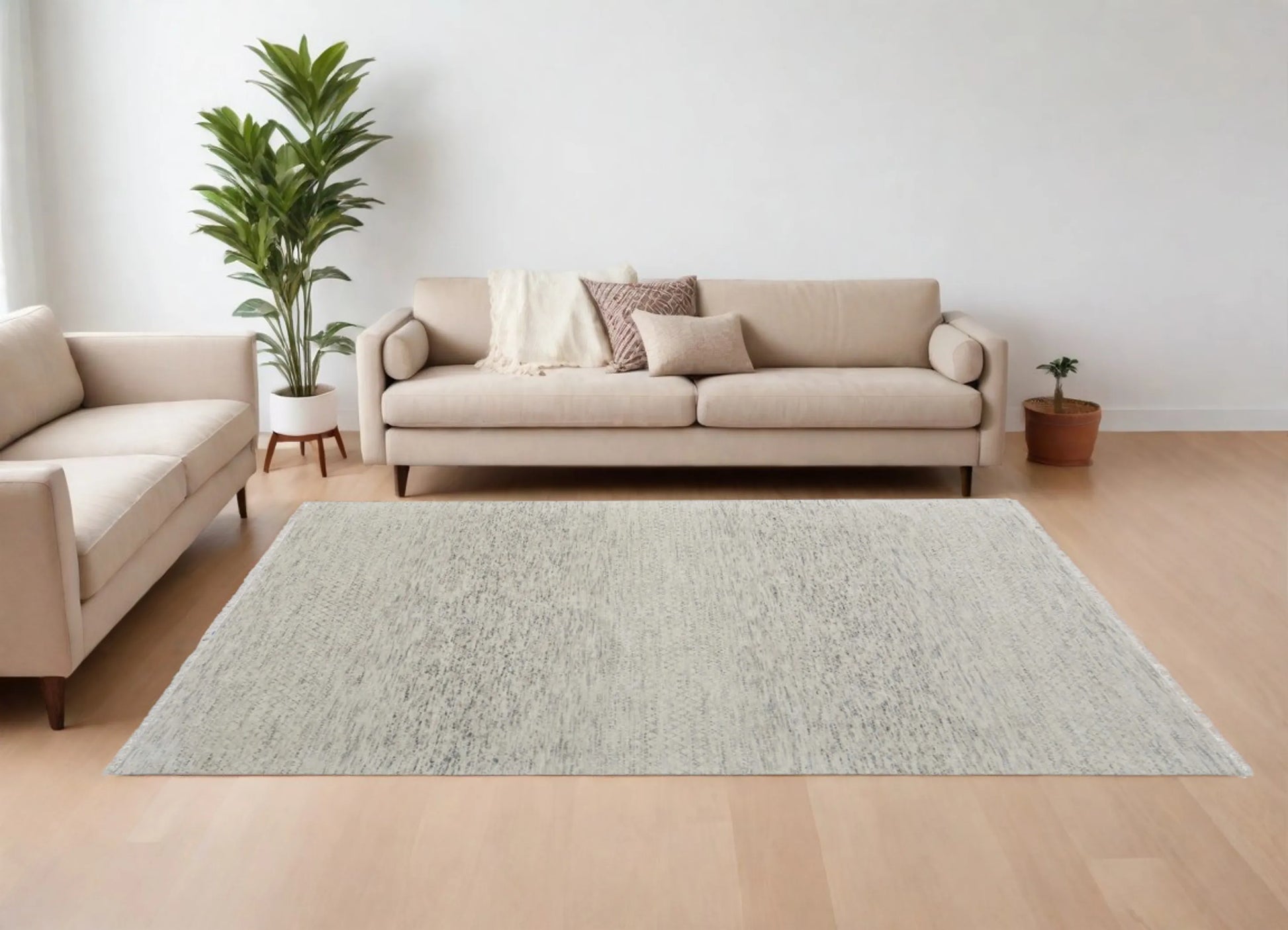 Living room with a beige sofa, gray wool rug, and decorative plants on a light wood floor.