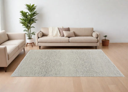 Living room with a beige sofa, gray wool rug, and decorative plants on a light wood floor.