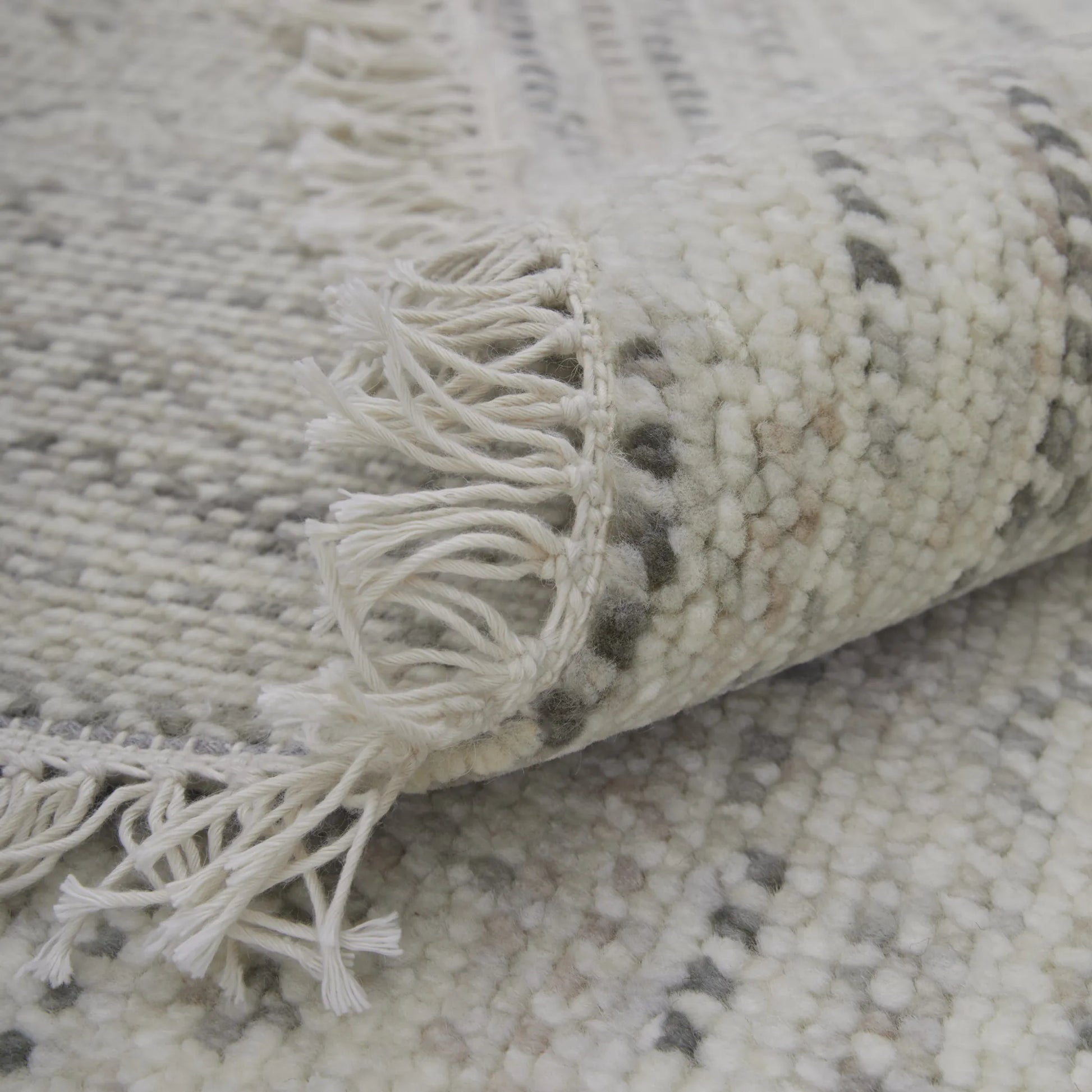 Close-up of a textured wool rug with fringes on a neutral background