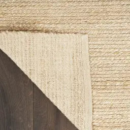 Close-up of a textured beige jute rug corner on a wooden floor