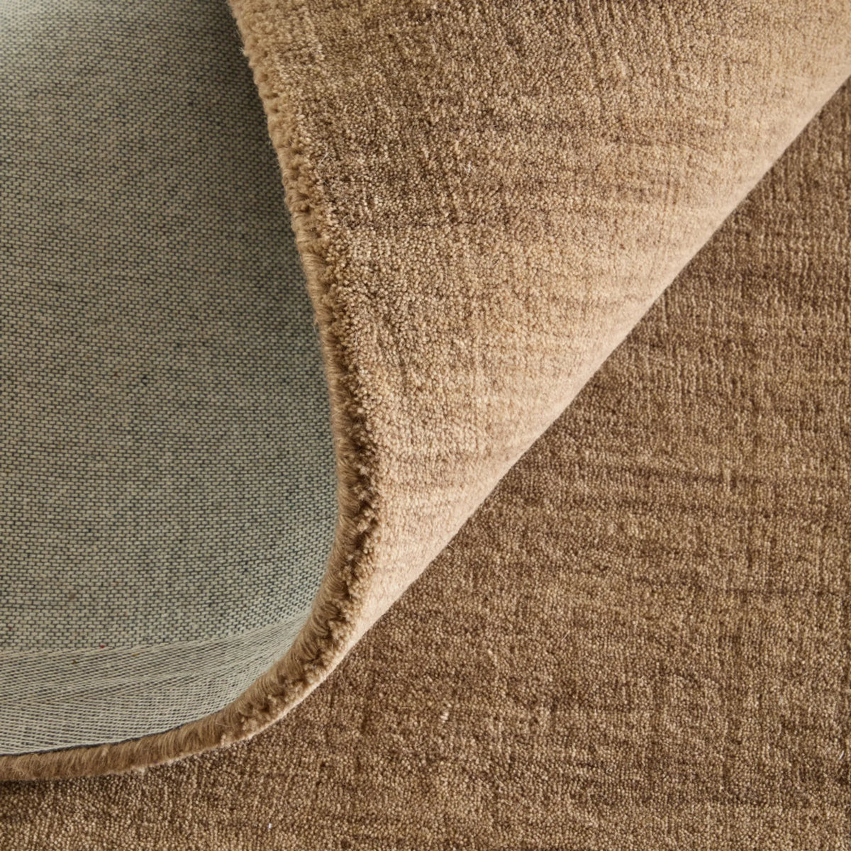 Warm tan wool rug with corner turned back to reveal backing