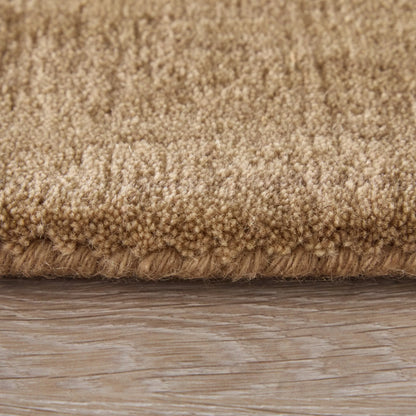 Close-up of a beige shag rug with a thick looped pile and fringed edge, shown resting on a light wood floor.