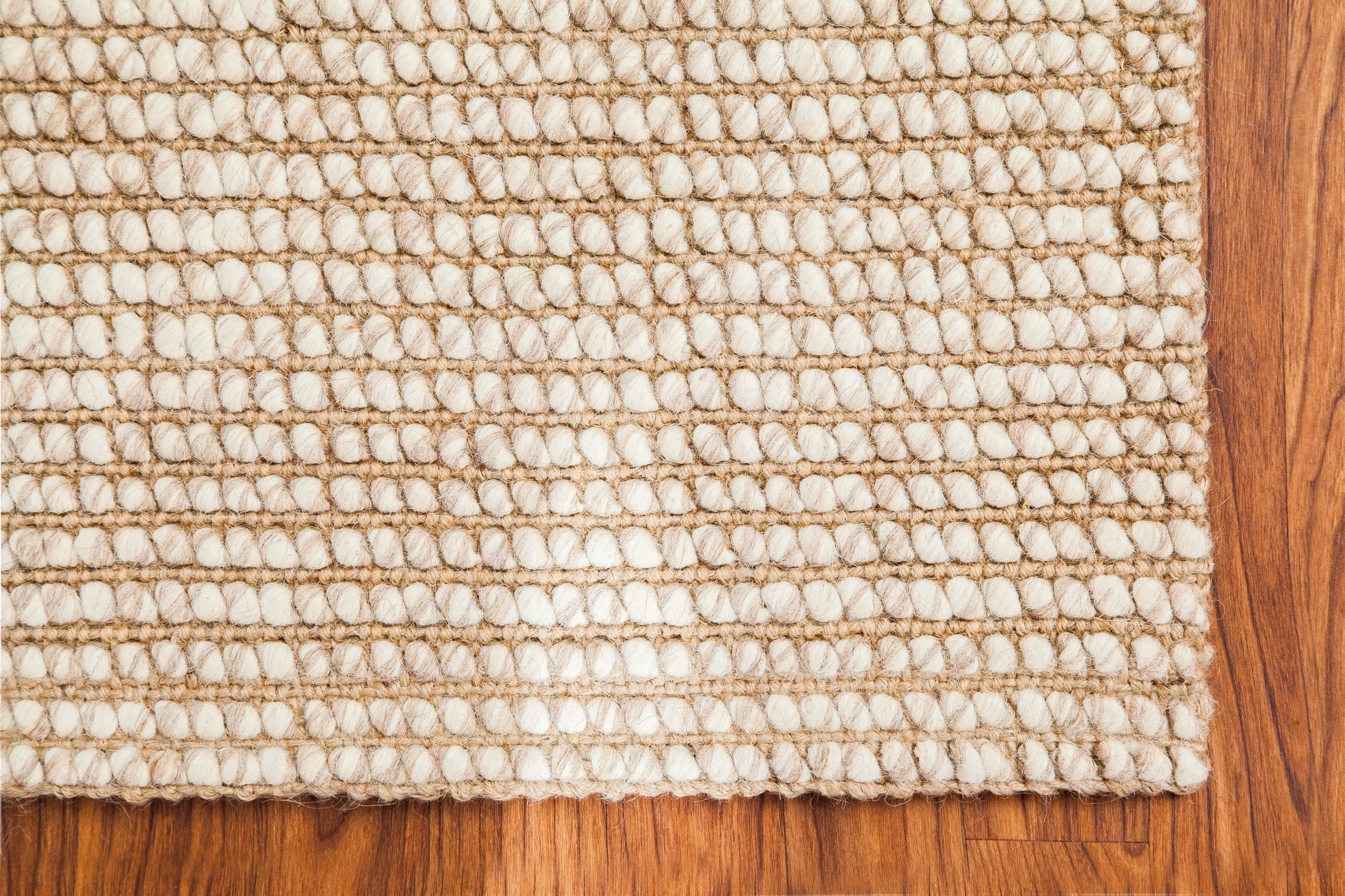 corner of woven ivory and beige rug on wood floor