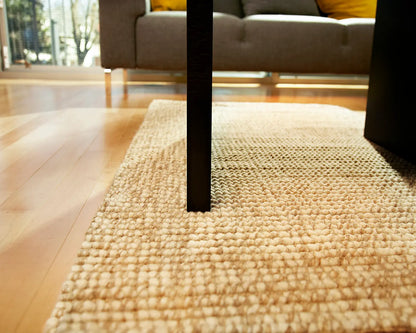 textured natural rug beneath a wooden table leg
