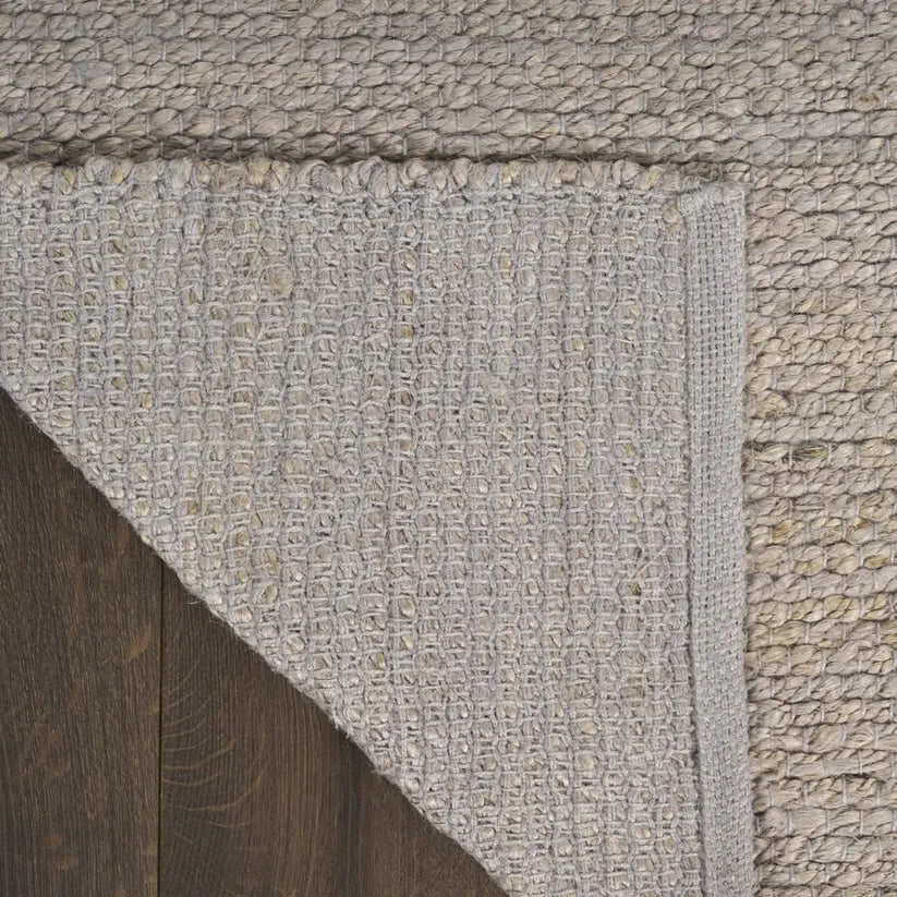 Close-up of a textured gray jute rug corner on a wooden floor